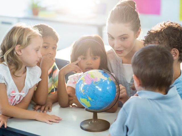 White female teacher speaking to a diverse group of students around a globe