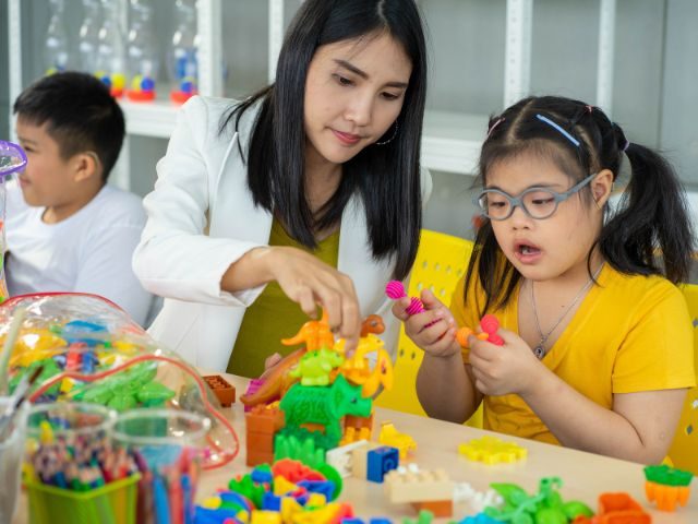 Female teacher using building blocks with child with disabilities