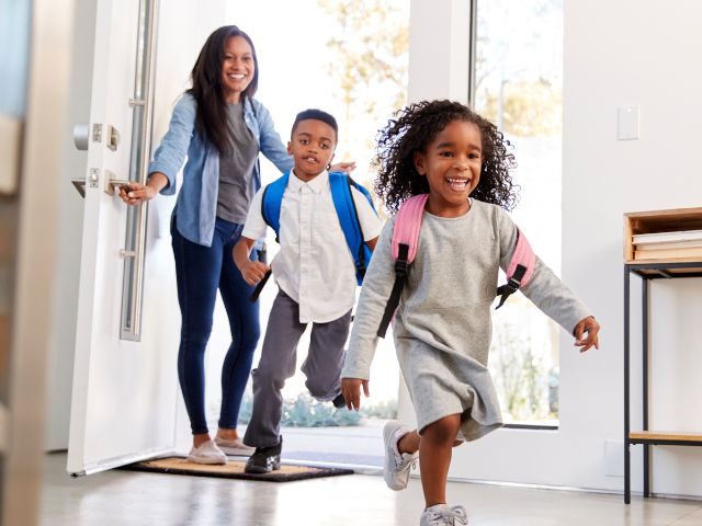 Black mother holding school door open for her two children