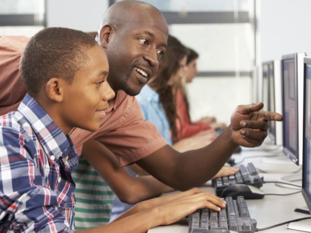 Black male teacher talking to student and pointing at computer